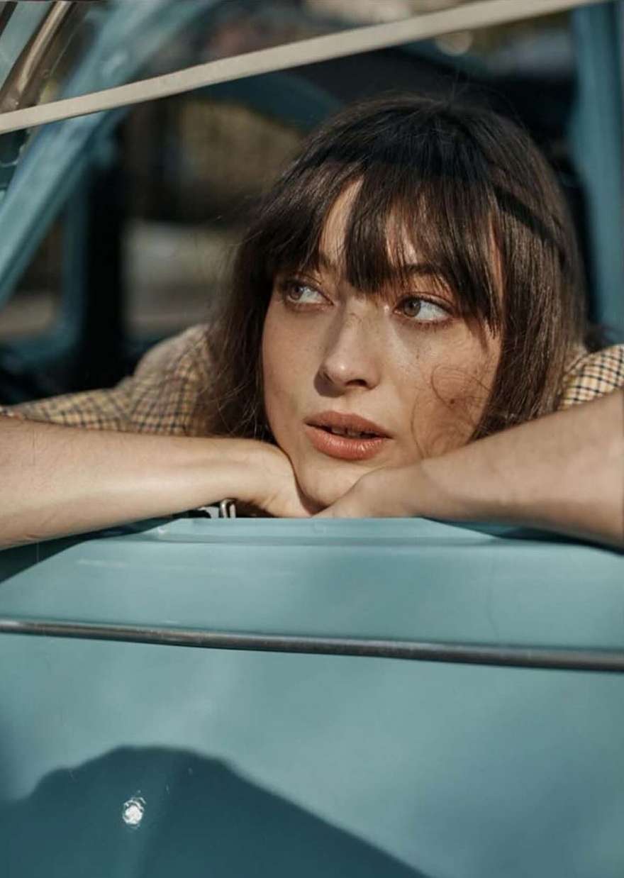 Close-up portrait of a woman resting her chin on her crossed arms leaning inside a blue vintage car.