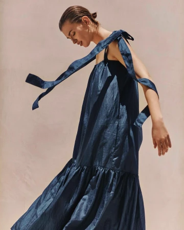 Model in a dark blue silk dress with shoulder ties captured in motion against a plain warm background