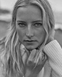Close-up monochrome portrait of a blonde woman resting her chin on her hand, wearing a textured white sweater.