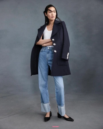 A full-length shot captures an Asian woman posing in a navy coat, white top, and blue jeans against a gray backdrop in a studio setting.