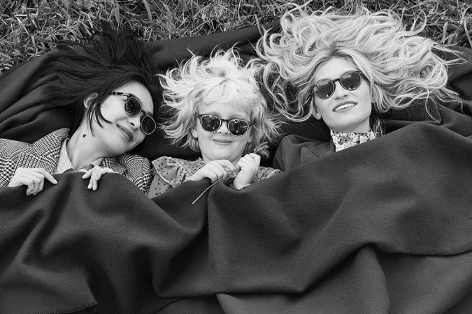 Three people lying down outdoors on a dark blanket wearing sunglasses, photographed in black and white by Coliena Rentmeester