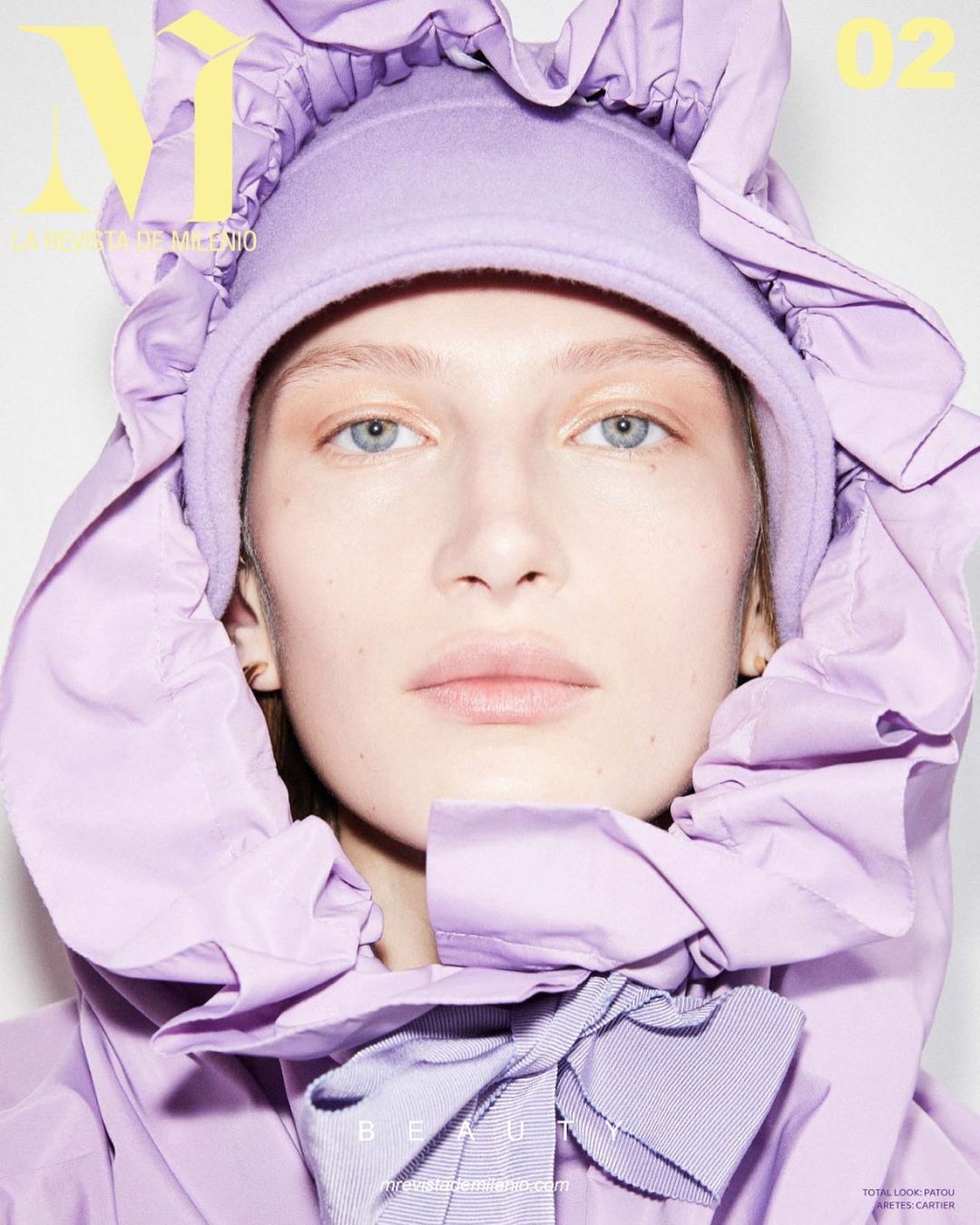 Fashion magazine cover featuring a fair-skinned woman in a lilac ruffled hooded jacket, with a ribbon, and soft studio lighting.