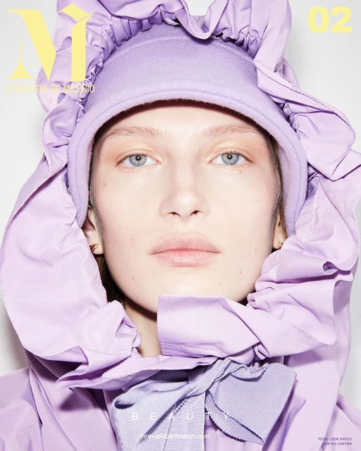 Fashion magazine cover featuring a fair-skinned woman in a lilac ruffled hooded jacket, with a ribbon, and soft studio lighting.