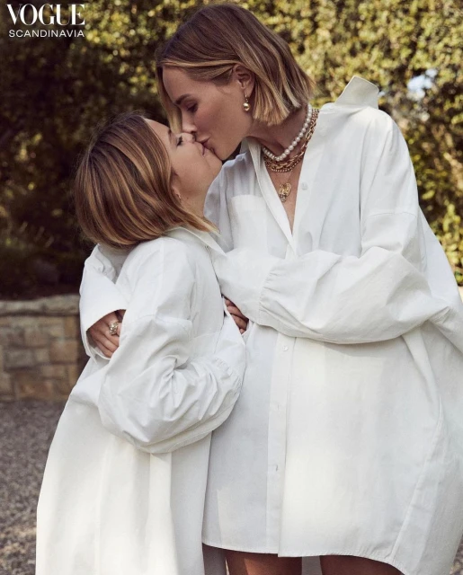 Two women in white oversized shirts embrace and kiss outdoors in a fashion editorial style. Vogue Scandinavia logo visible.