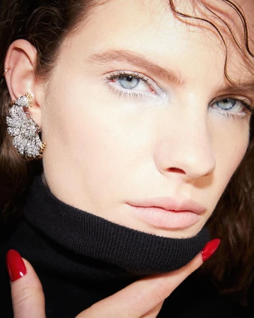 Close-up of a woman with fair skin and blue eyes wearing a black turtleneck and a large ornate earring, showcasing beauty and fashion.