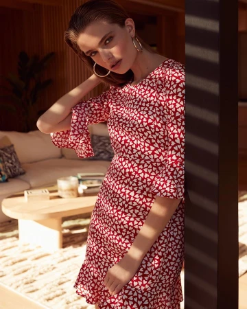 A fashionable young woman in a red and white heart-print dress poses in an interior setting with a neutral color palette and soft lighting.
