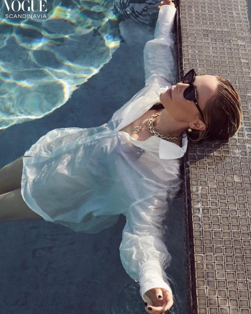 Woman in a white shirt and sunglasses relaxes in a swimming pool with light reflecting on the water, photographed for Vogue Scandinavia.