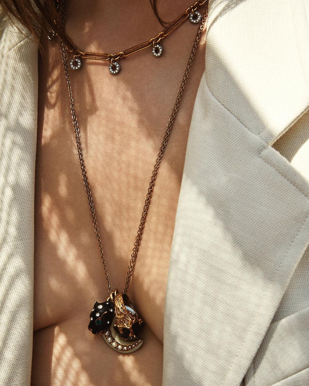 Close-up of a woman wearing several necklaces with pendants, and a light-colored jacket, showcasing fashion and jewellery.