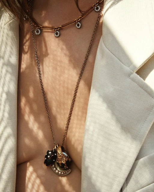 Close-up of a woman wearing several necklaces with pendants, and a light-colored jacket, showcasing fashion and jewellery.