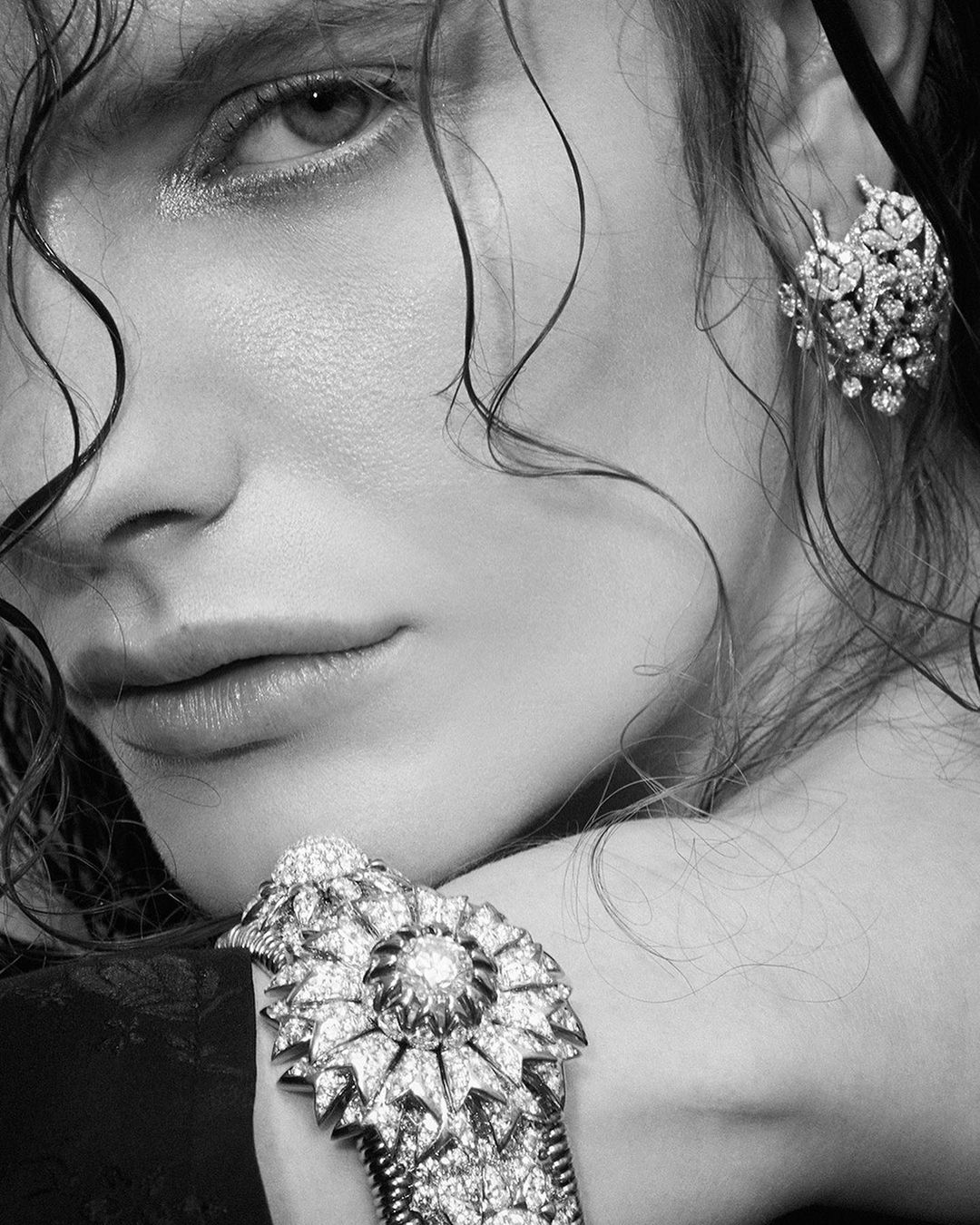 Close-up monochrome portrait of a model with wet hair wearing sparkling diamond earrings and a matching bracelet