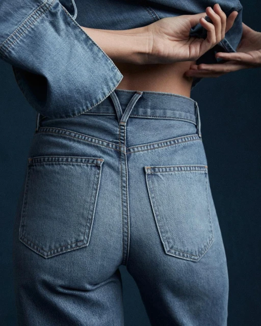 Back view of a person wearing denim jeans and a matching denim jacket, posing in a studio environment with a dark background.