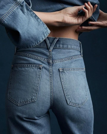 Back view of a person wearing denim jeans and a matching denim jacket, posing in a studio environment with a dark background.