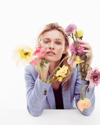 A female model posing with colorful flowers emerging from her blue blazer sleeves against a white background.