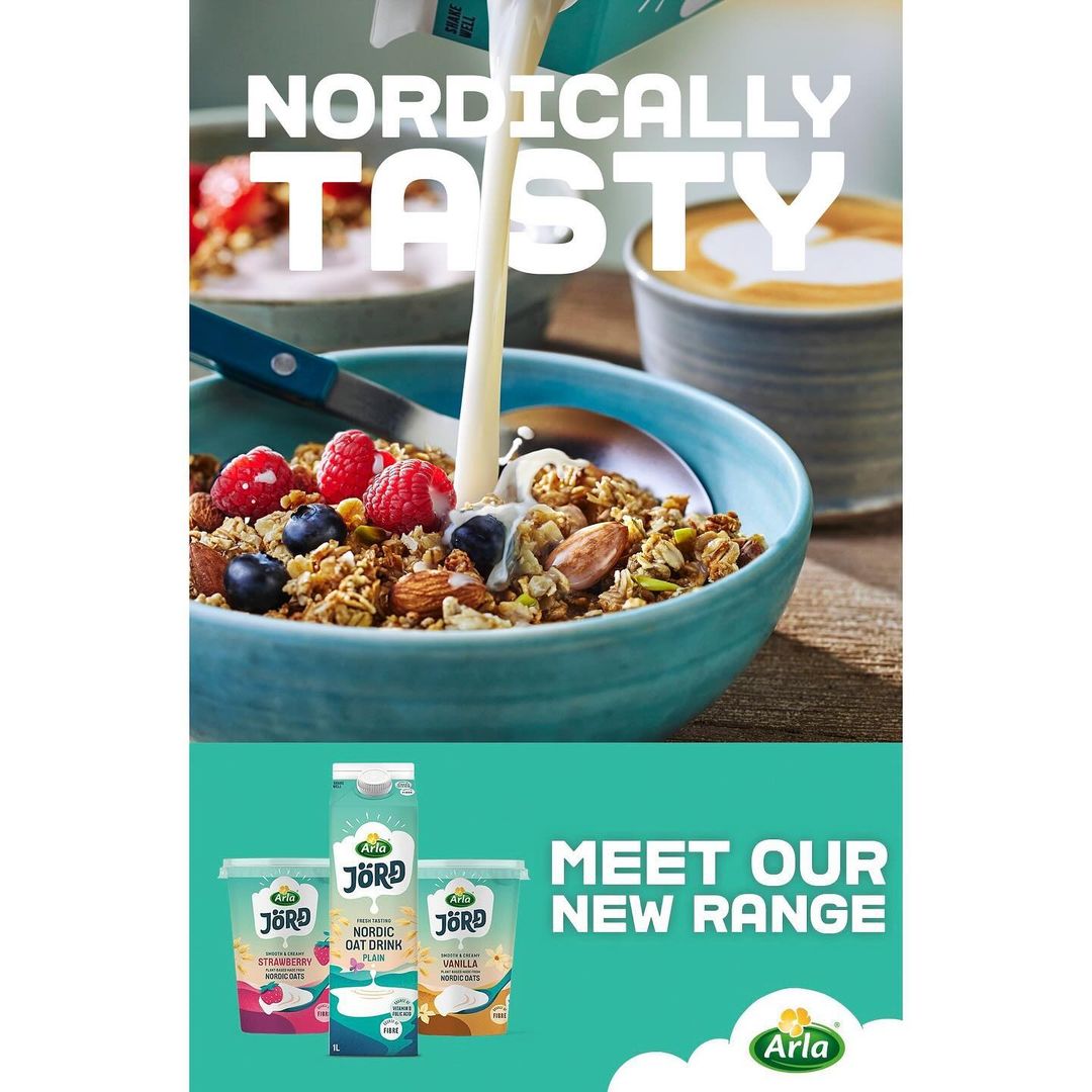 Overhead shot of milk pouring into a turquoise bowl of granola with berries; Jörd Nordic oat drink products below.