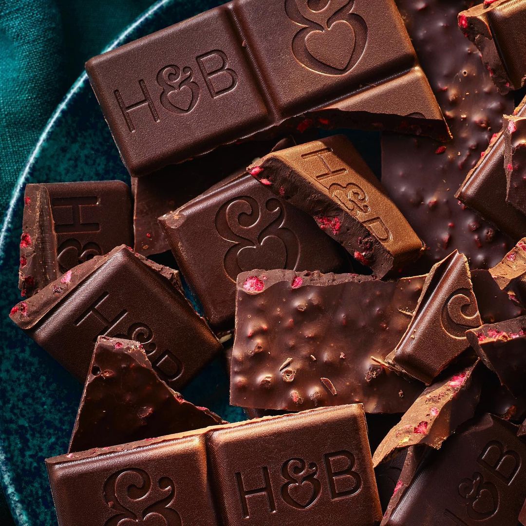 Close-up of assorted dark chocolate pieces with embossed designs on a dark teal plate, showcasing textures and rich brown hues.