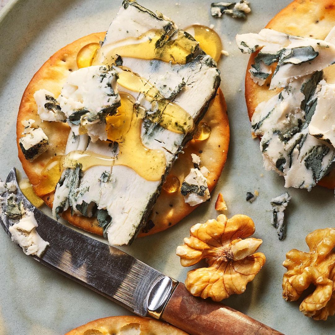Overhead shot of gourmet blue cheese on crackers drizzled with honey alongside walnuts on a light blue plate, close-up, studio shot.