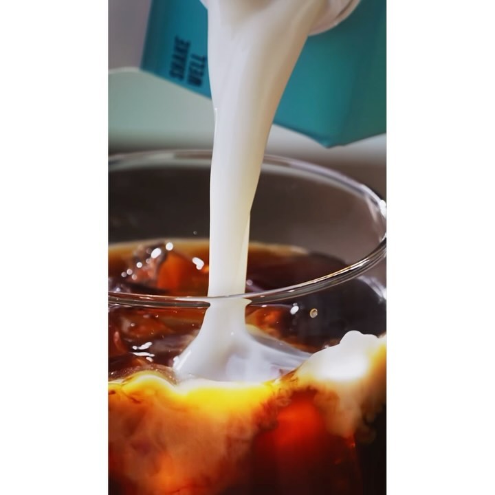 Milk pouring into a glass of iced coffee with ice cubes, creating a visually appealing beverage with a mix of dark and light tones.