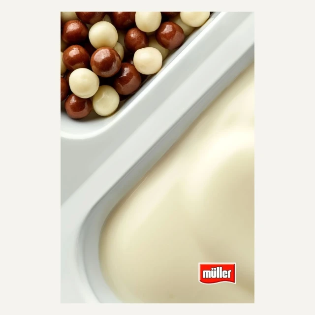 High-angle studio shot of a white plastic container featuring creamy white yogurt on one side and chocolate & cream-filled balls on the other.