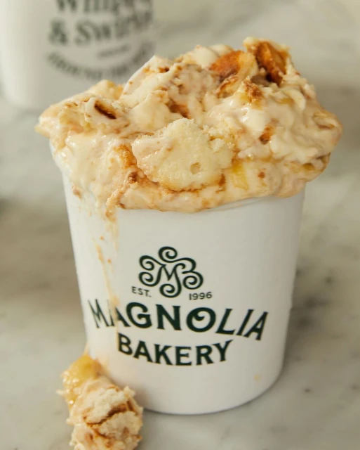 Magnolia Bakery banana pudding in a cup with logo on marble surface, rich in creamy texture and golden hues, food photography.
