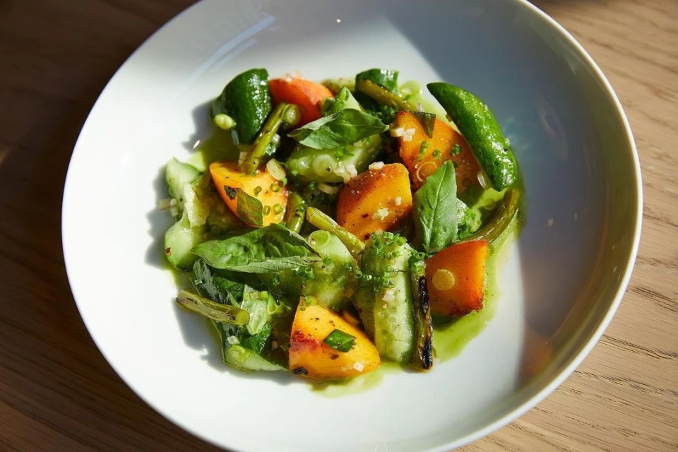 Close-up overhead shot of a fresh salad on a white plate with tomatoes, basil, cucumbers, and scallions, drizzled with a green sauce.