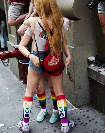 Two people stand wearing rainbow and LOVE-themed socks with a red backpack in an outdoor urban setting.