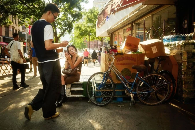 Man and woman standing on a New York sidewalk near stacked cardboard boxes and a blue bicycle, photographed by Colin Clark.