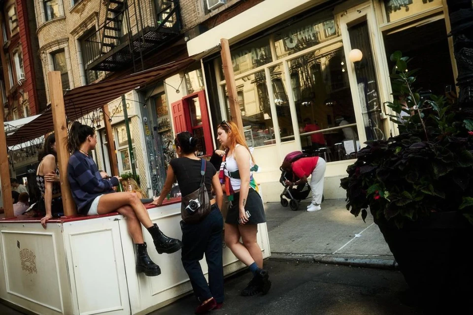 Several women gather outside a city cafe with a red awning, featuring outdoor seating, offering a glimpse into urban social life.
