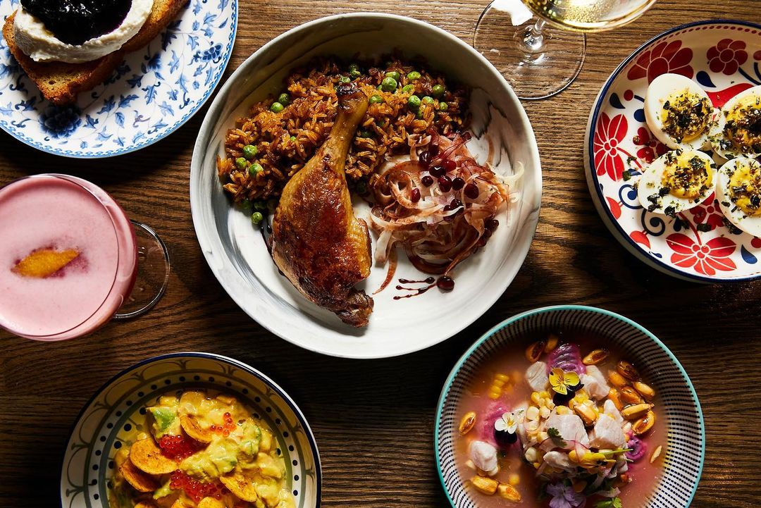 Overhead shot of beautifully arranged dishes on a wooden table, featuring duck leg, rice, a cocktail, and various appetizers.