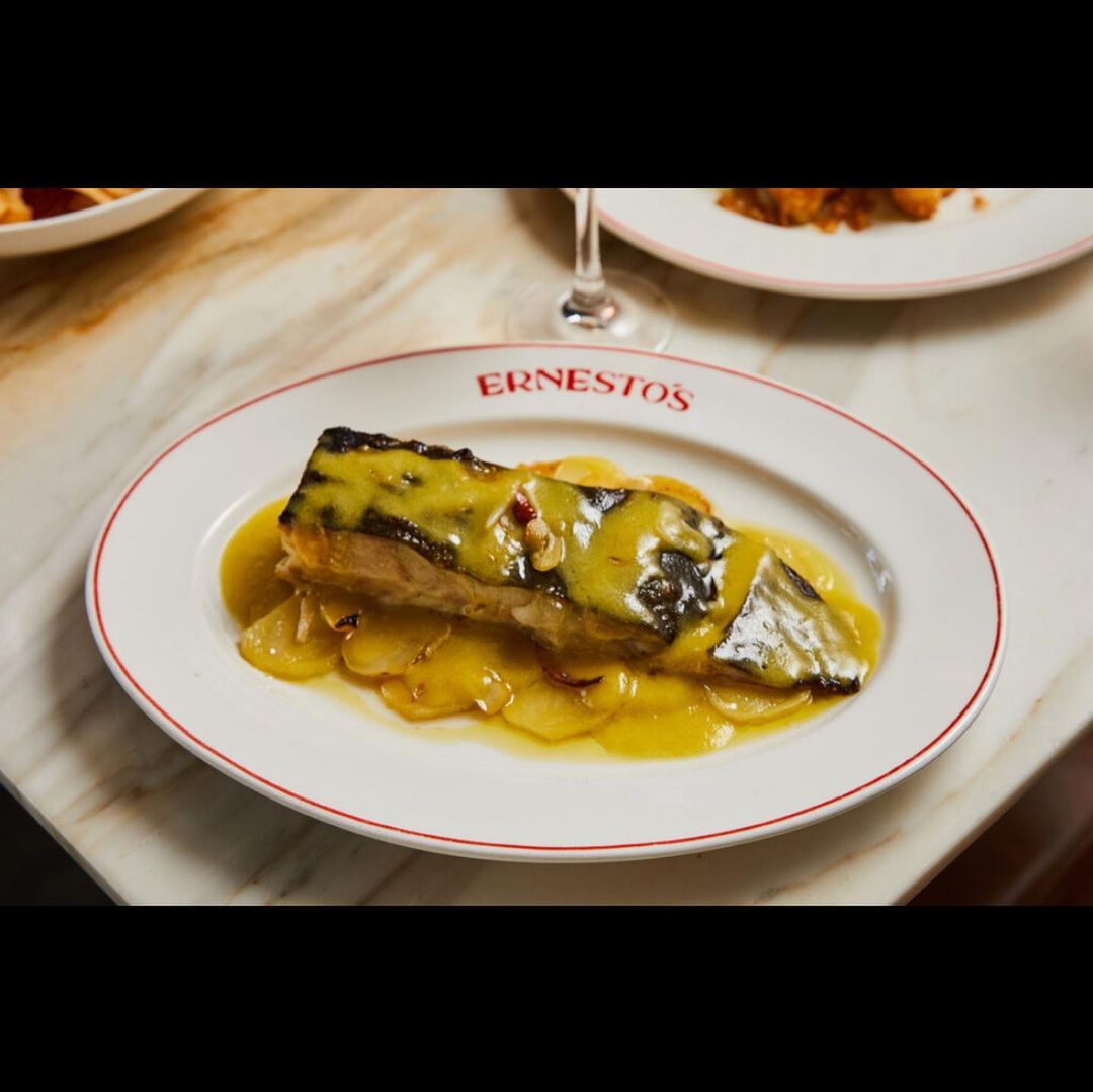 Close-up of plated fish dish with sliced potatoes and yellow sauce on a white plate with red trim, resting on a marble table.