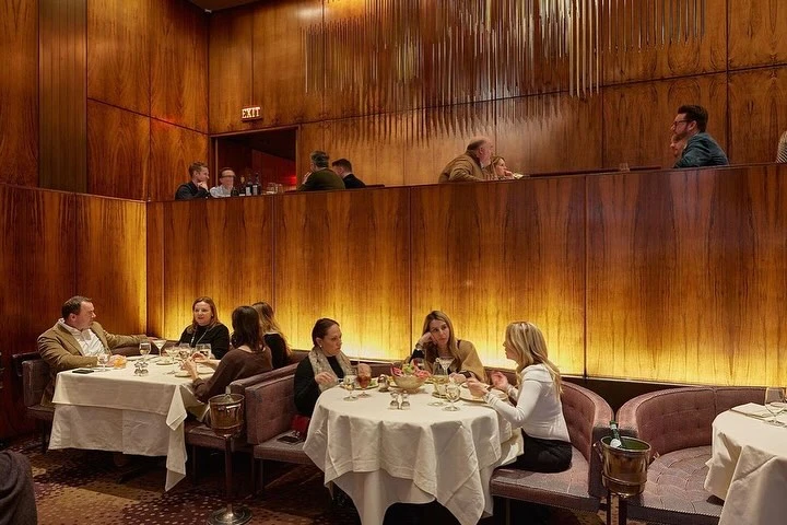 People dining in an upscale restaurant featuring wood-paneled walls and tables covered with white tablecloths, creating an intimate setting.