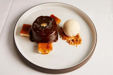 Chocolate dessert with caramel sauce, gold leaf, sliced bananas, and ice cream on a plate by Colin Clark