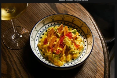 A decorative ceramic bowl of Peruvian ceviche garnished with plantain chips and red roe, next to a wine glass on a dark wooden table.
