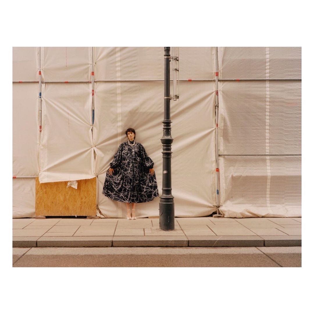 Fashion photography of a woman in a black and white patterned dress standing on a sidewalk against a white construction wall.