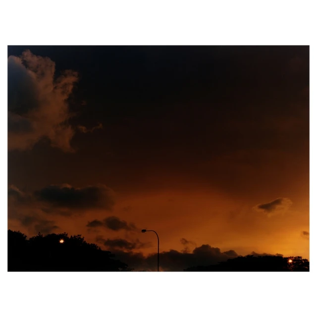 Dramatic sunset sky with orange and black hues, silhouetted trees, and a solitary street lamp providing a serene yet striking contrast.