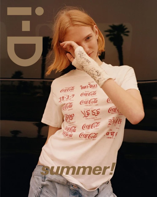 A redhead woman in a Coca-Cola t-shirt with an arm cast poses against a car with a palm tree backdrop in this fashion editorial.