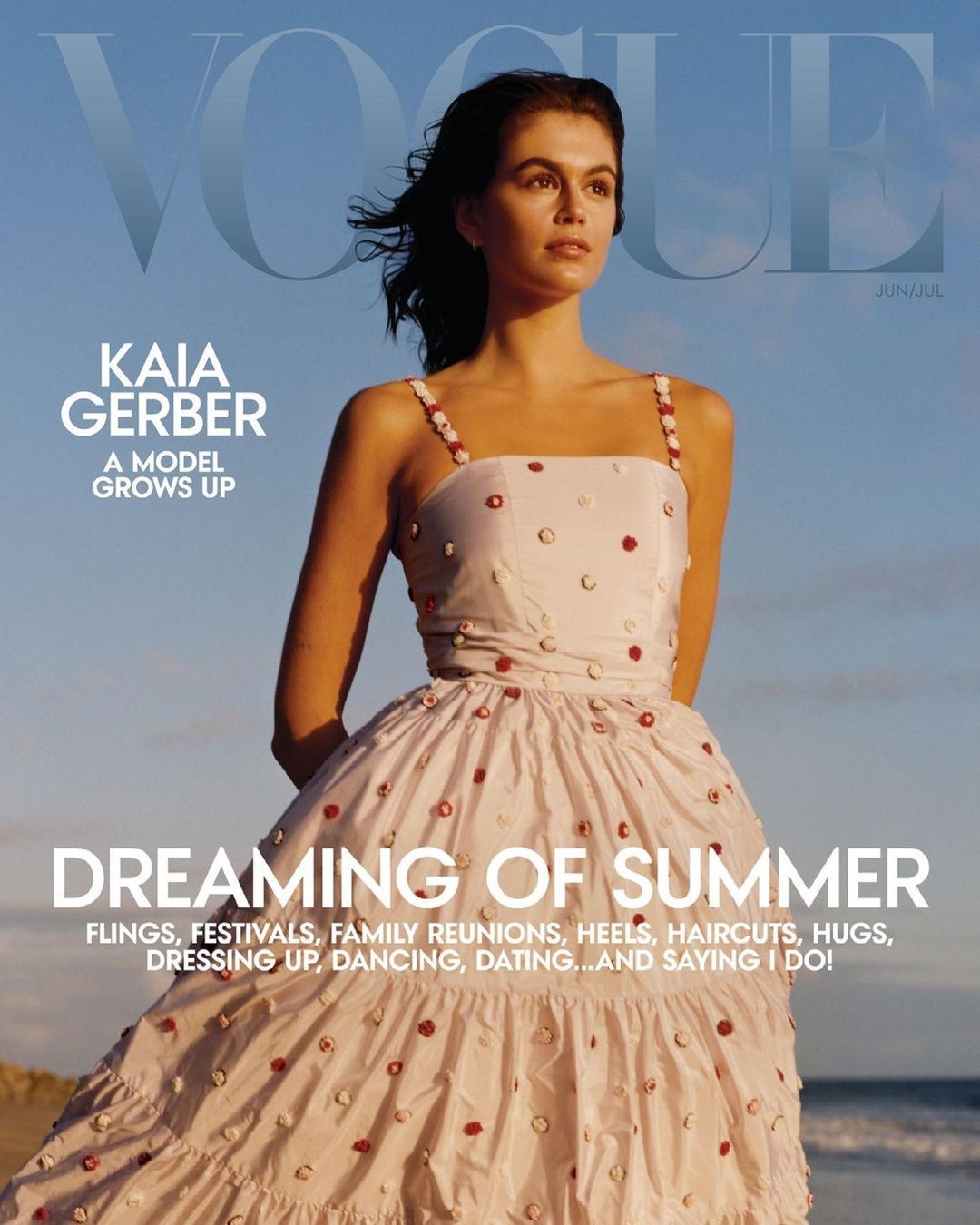 Vogue cover featuring Kaia Gerber in a white dress with red embellishments, set against a blue sky and sandy beach.