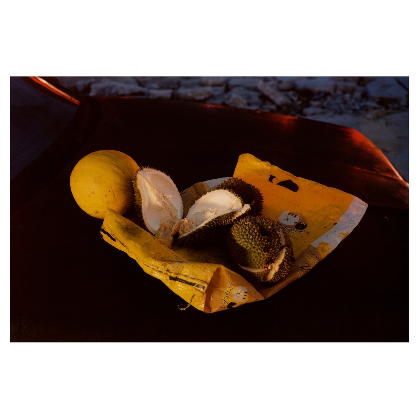 Durian and yellow melon on a yellow cloth against a dark background. The durian is partially open, revealing the fruit inside.