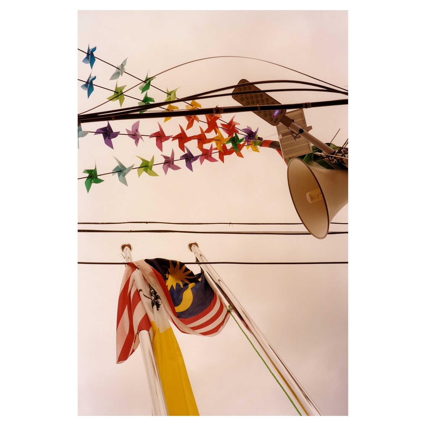 Low-angle shot featuring flags, a loudspeaker, and rainbow origami birds against a light-colored sky, creating a unique, colorful scene.
