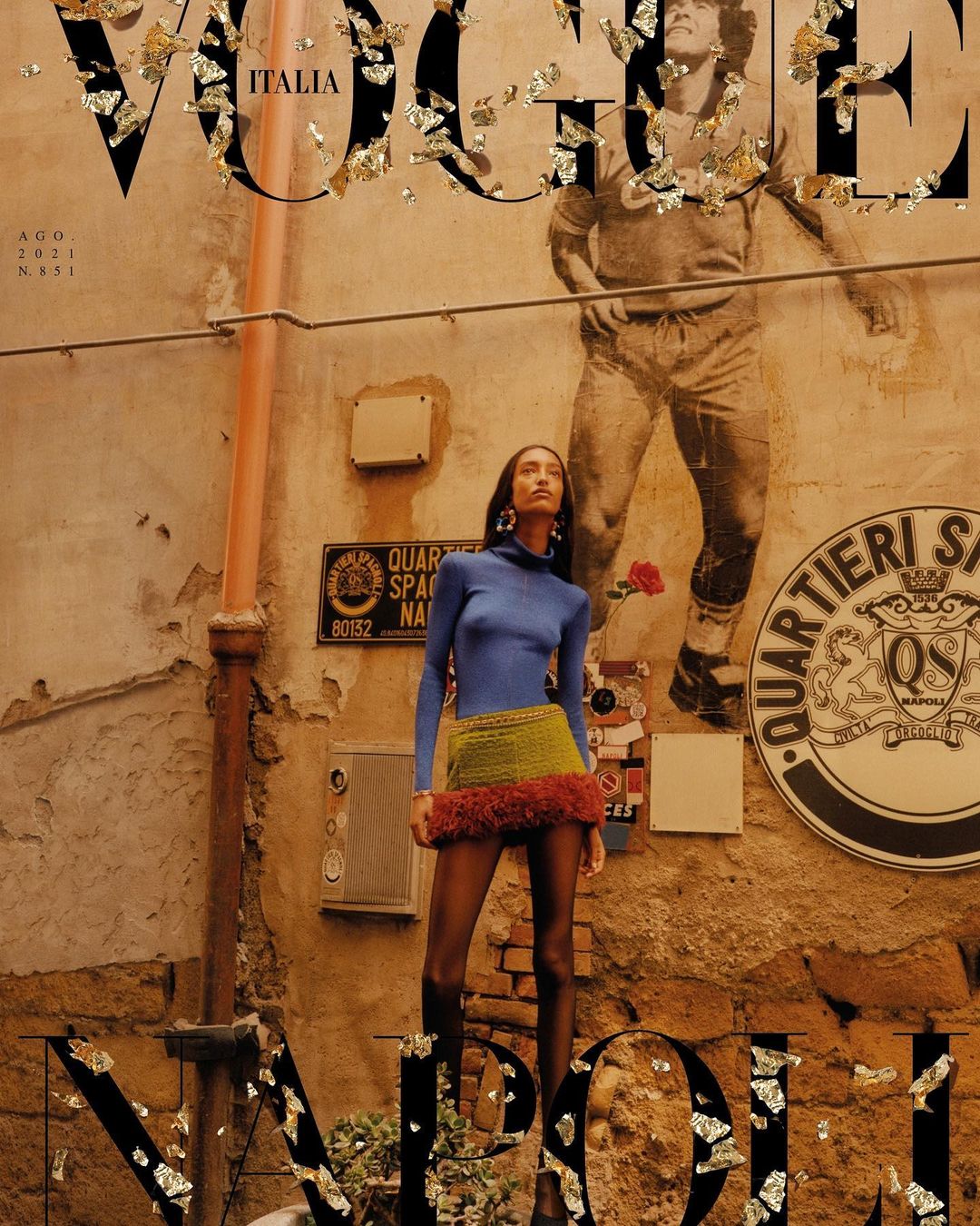 Vogue Italia cover featuring a fashion model in a blue long-sleeve top and knit skirt, standing in an urban alleyway with vintage walls.