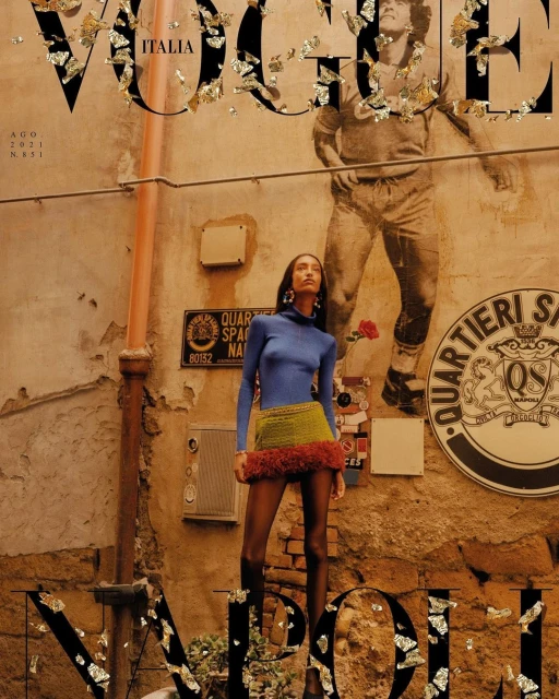 Vogue Italia cover featuring a fashion model in a blue long-sleeve top and knit skirt, standing in an urban alleyway with vintage walls.