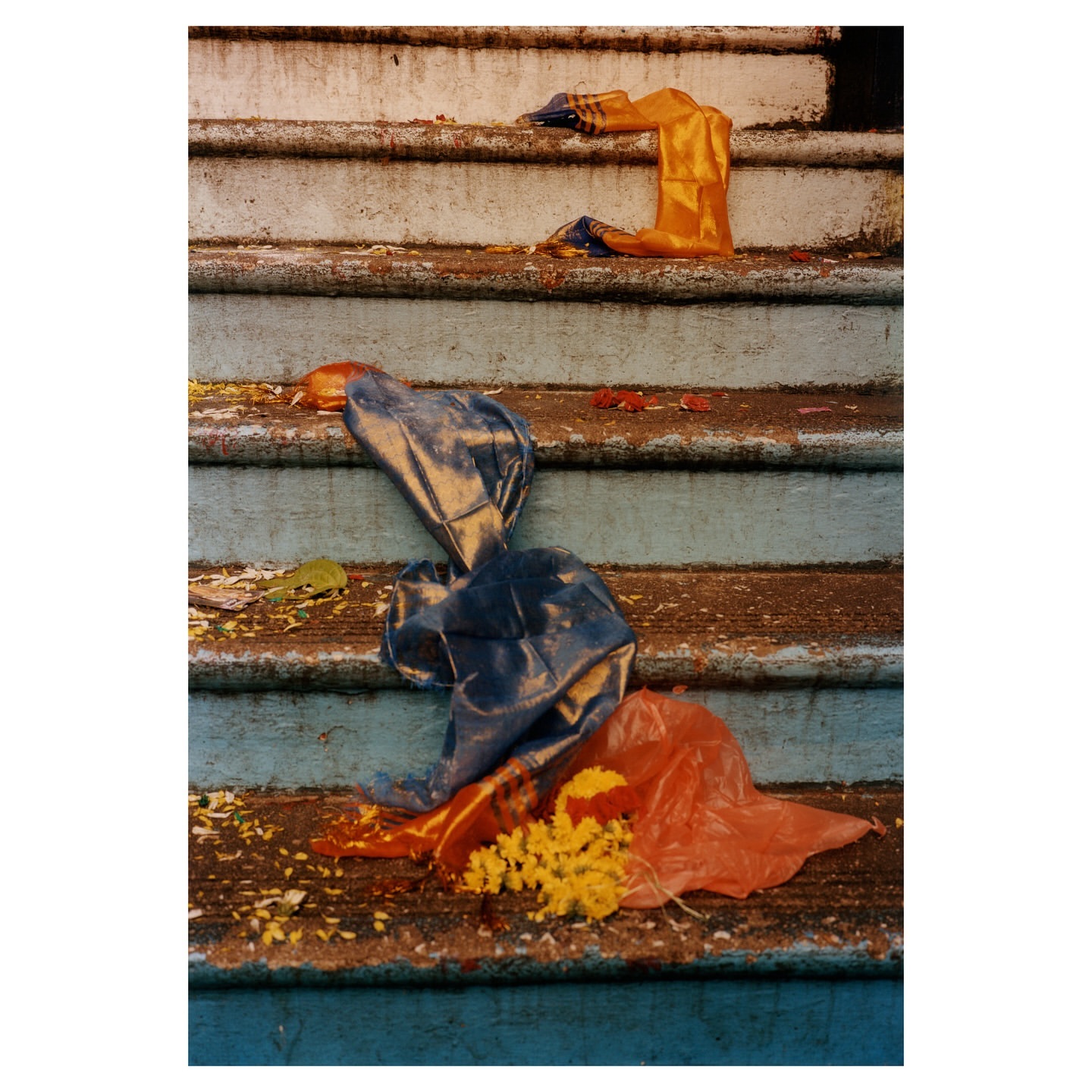 Discarded colorful plastic bags and yellow flower petals litter the weathered concrete steps of an outdoor staircase with chipped paint.