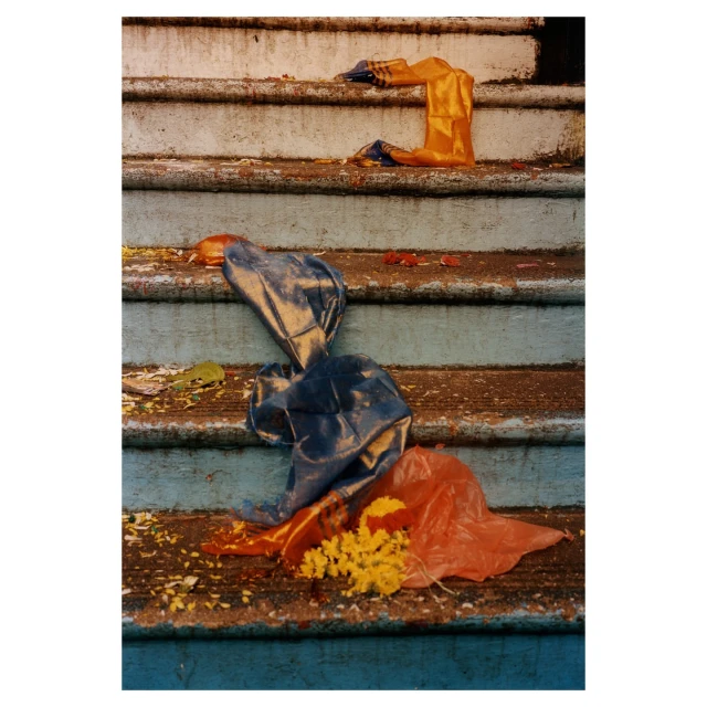 Discarded colorful plastic bags and yellow flower petals litter the weathered concrete steps of an outdoor staircase with chipped paint.
