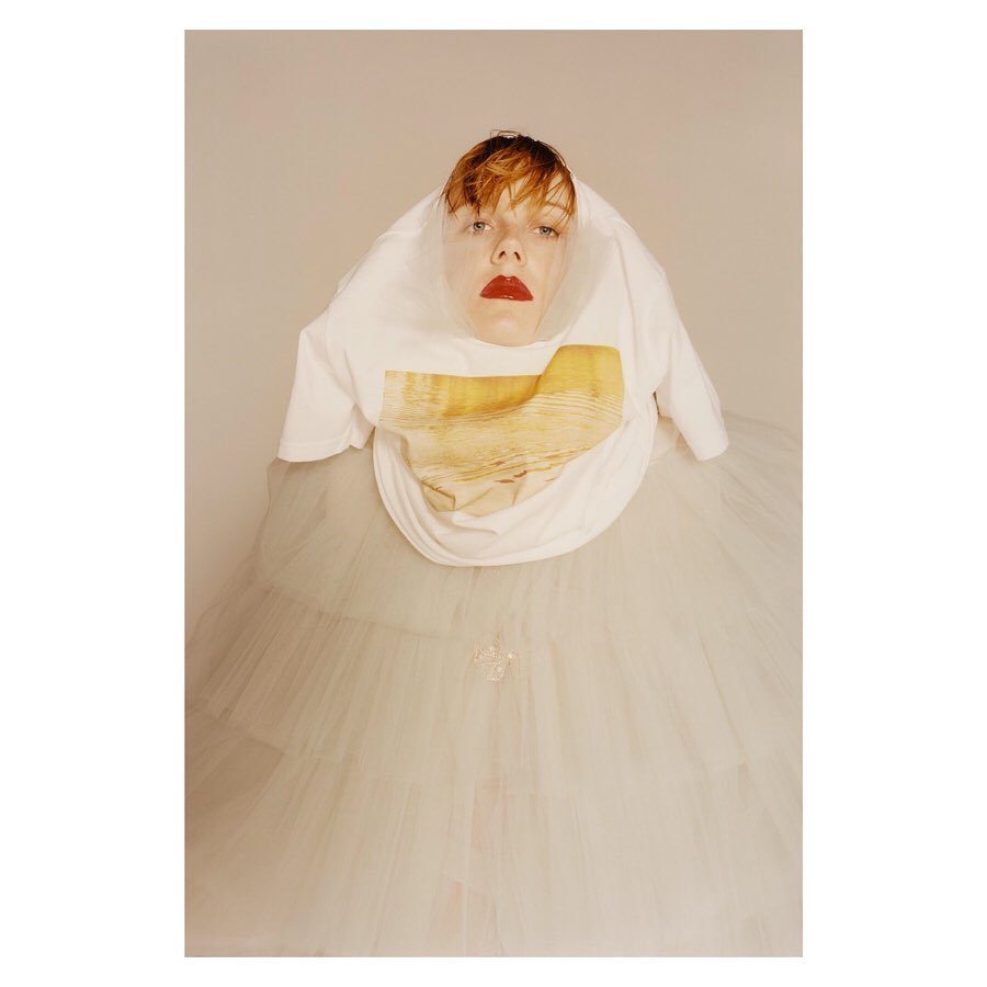 Woman in a white t-shirt and a sheer, puffy skirt strikes a pose, creating a surreal and whimsical visual with soft, diffused lighting.