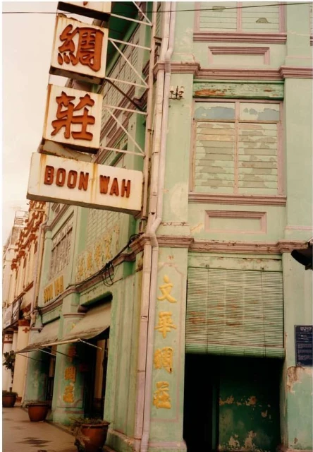 An old building in Asia with faded green paint and weathered signs in Chinese characters, showcasing vintage architecture.