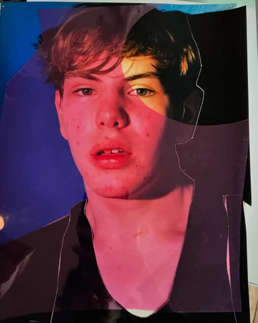 Artistic collage portrait of a young adult male's face, constructed from layered and torn paper fragments against a blue backdrop.