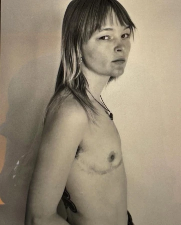 Monochrome portrait of a person with shoulder-length layered hair and bangs looking back over their shoulder against a plain background
