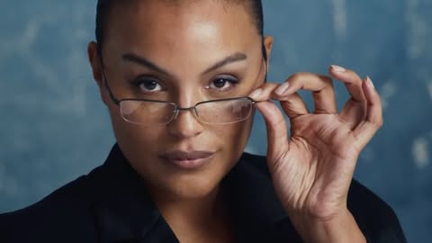 Portrait of a dark-skinned woman with glasses adjusting her frames, close-up shot with a muted blue background, focusing on her confident gaze.