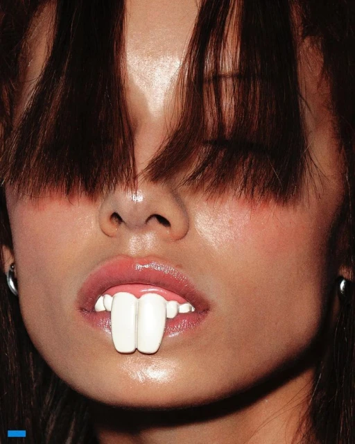 Close-up of a young adult female with dark brown hair and fair skin, featuring two large, white, rectangular objects in her mouth.