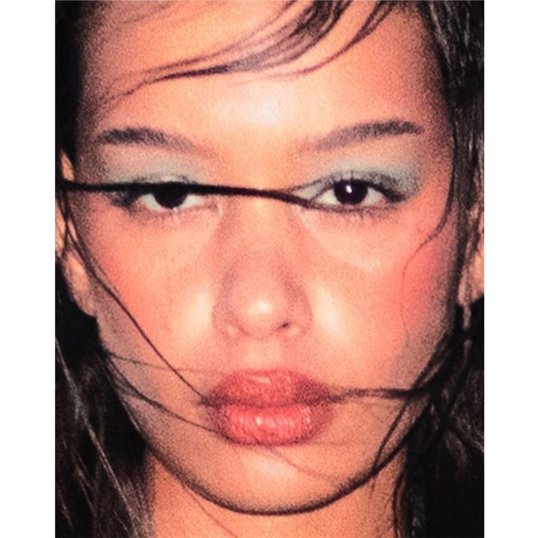 Close-up portrait of a woman with wet hair framing her face, wearing blue eyeshadow and light red lipstick, by Conor Cunningham.