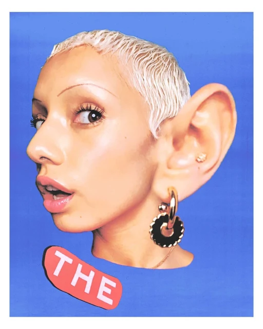 Woman with short white hair and large ears poses against a blue background, wearing gold hoop earrings and a black statement earring.